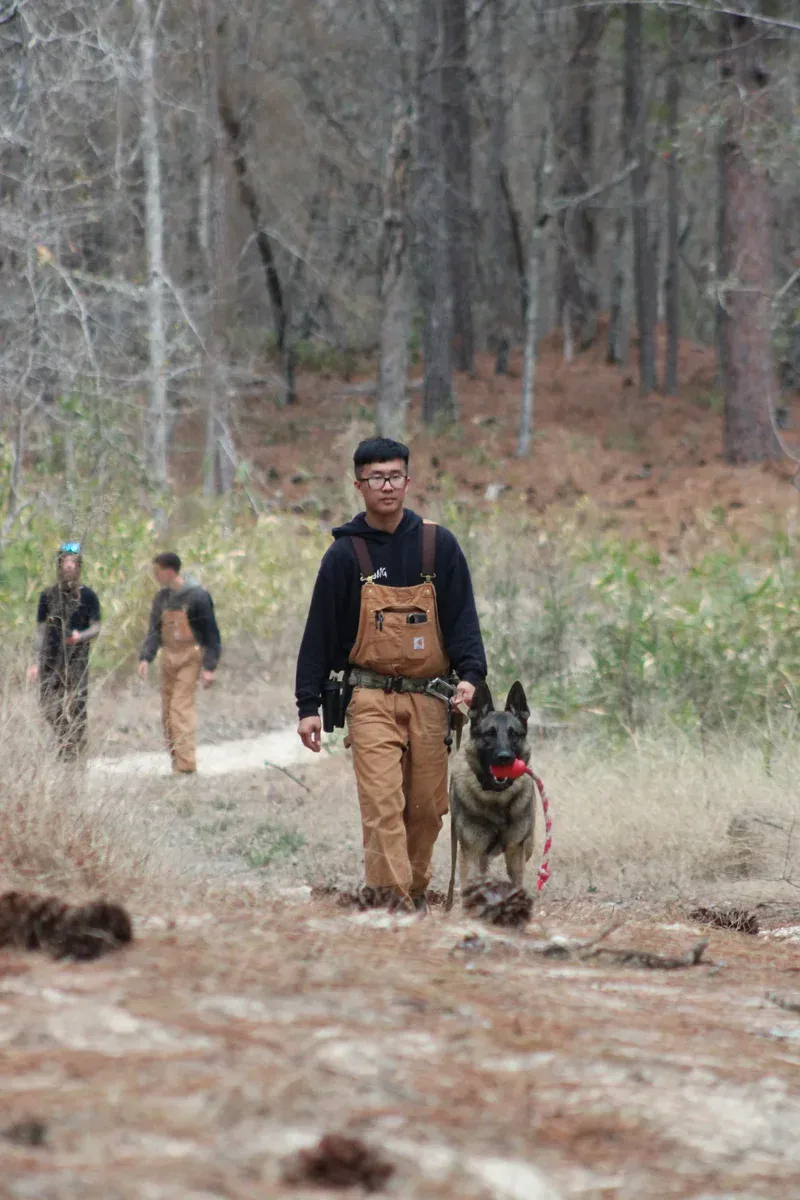 Young man hiking with service dog in wooded trail outdoors.
